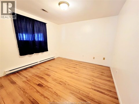 A room with wooden flooring and a window with black curtains.