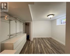 A room with wooden flooring and white walls, with a window on the right wall.