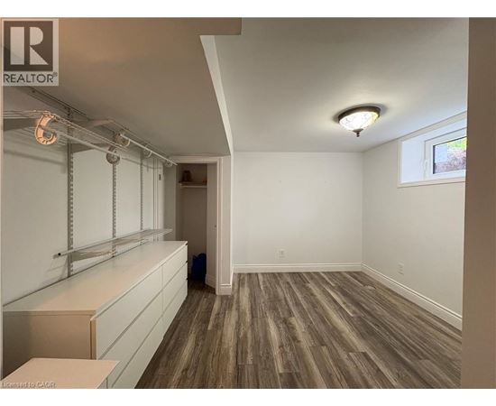 A room with wooden flooring and white walls, with a window on the right wall.