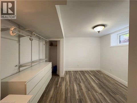 A room with wooden flooring and white walls, with a window on the right wall.