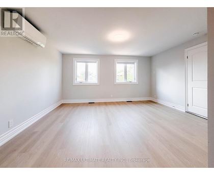 A spacious room with wooden flooring and two windows.