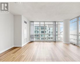 A spacious room with wooden floors and a large window overlooking a building.