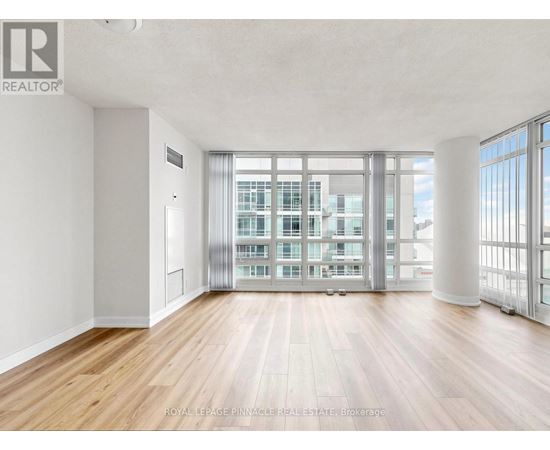 A spacious room with wooden floors and a large window overlooking a building.