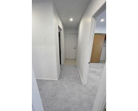 A long, narrow hallway with white walls and carpeted floor.