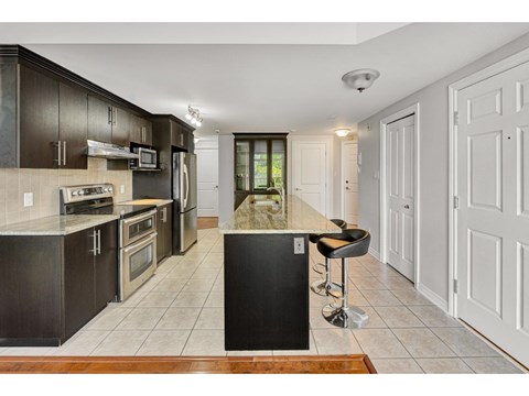 A kitchen with dark brown cabinets and a black island.