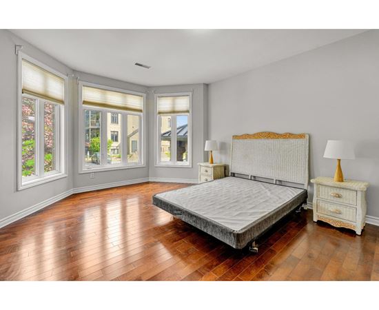 A bedroom with a large bed, wooden floors, and a window with blinds.