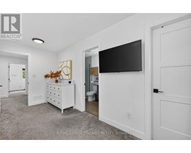A white bedroom with a dresser and a flat screen TV mounted on the wall.