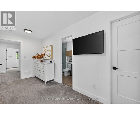 A white bedroom with a dresser and a flat screen TV mounted on the wall.