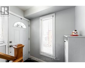 A white room with a door, a window with blinds, and a small table with a figurine on it.