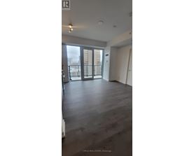 A spacious room with wooden flooring and a balcony with a view of buildings outside.