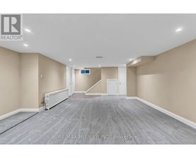 A spacious room with a carpeted floor and a staircase in the background.