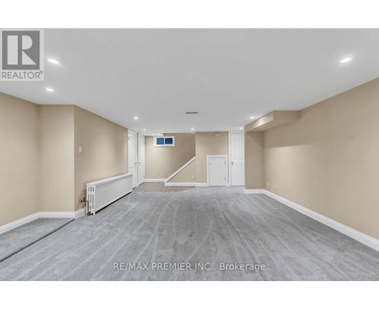 A spacious room with a carpeted floor and a staircase in the background.