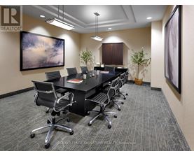 A conference room with a long table and chairs, a painting on the wall, and a carpeted floor.