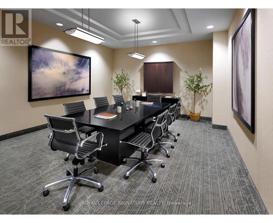 A conference room with a long table and chairs, a painting on the wall, and a carpeted floor.
