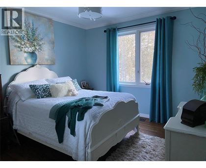 A bedroom with a white bed and a painting on the wall.