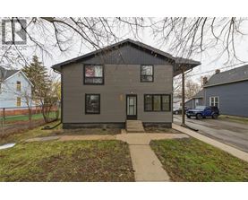 A grey house with a black roof and a small front yard.