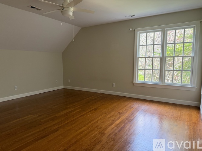 A room with a ceiling fan and a window with a view of trees.