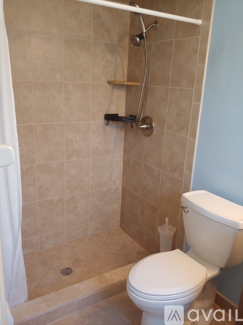 A beige tiled shower with a white toilet and a white shower curtain.