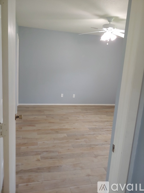A room with a ceiling fan and light and wood flooring.