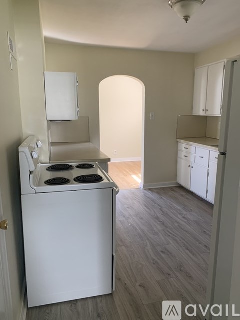 A white stove is in a kitchen with wood floors and white cabinets.