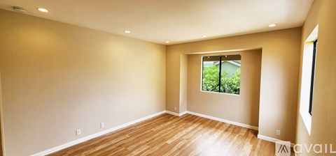 A spacious room with wooden floors and a window overlooking greenery.