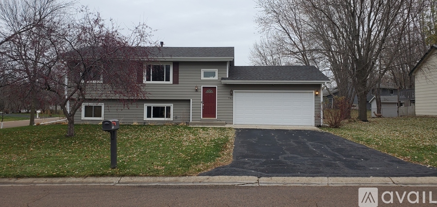 A grey house with a red door and a mailbox in front.