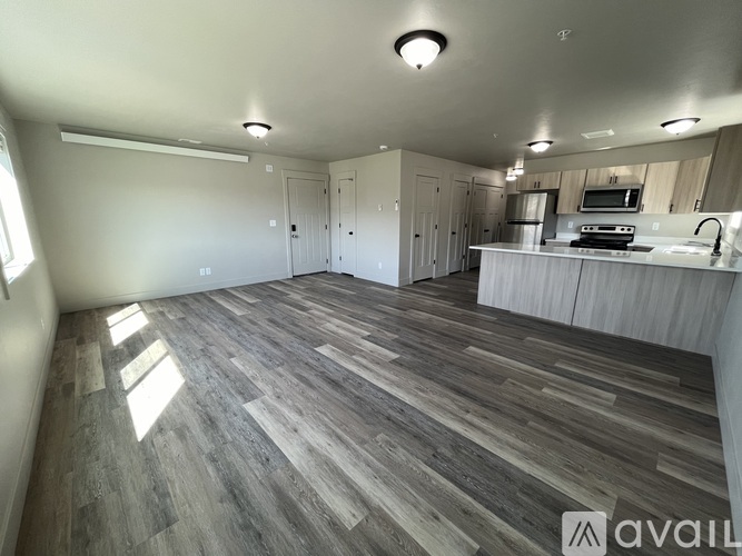 A spacious room with wooden flooring and a kitchen area with a sink and stove.