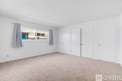 A room with white walls and a carpeted floor with a window and curtains.