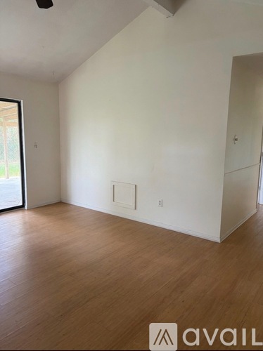 A room with wooden floors and white walls, with a window on the left and a door on the right.
