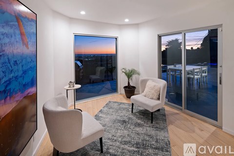 A living room with a large painting on the wall and a view of the city at dusk through the window.