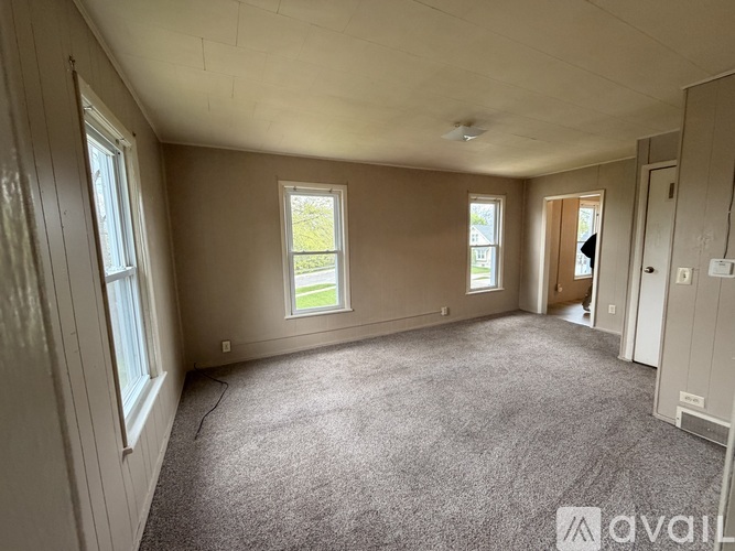 A spacious room with carpeted floor and three windows.