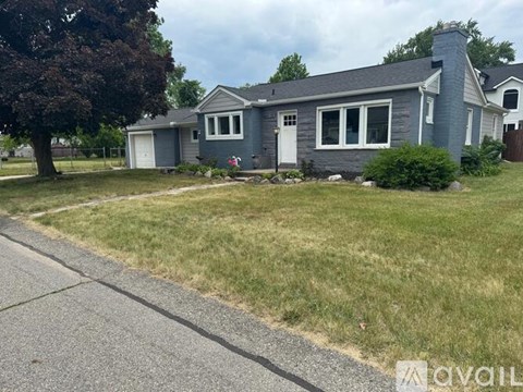 A grey house with a white door and windows is surrounded by a grassy area and a sidewalk.