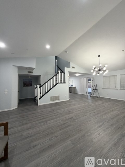 A spacious living room with a staircase and a chandelier.