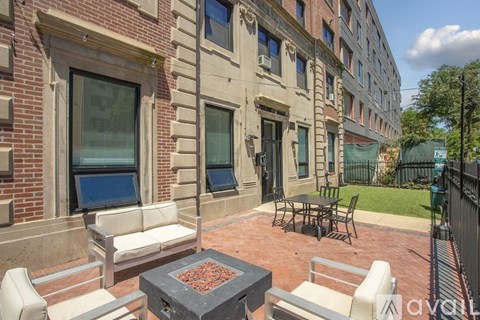 A patio with a fire pit and chairs is surrounded by a brick building.