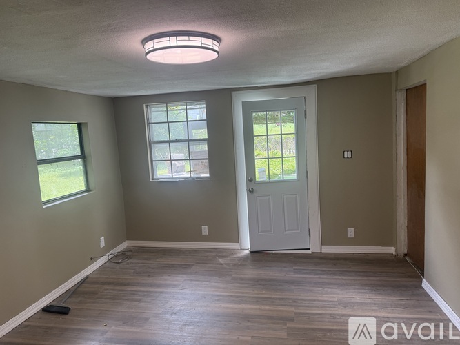 A room with a white door, two windows, and wooden flooring.
