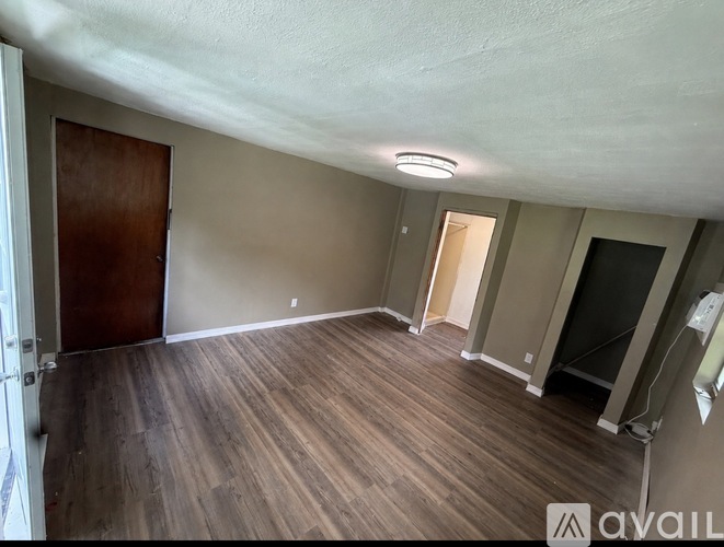 A room with wooden flooring and a door on the left side.