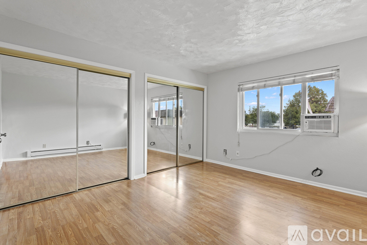 A room with a wooden floor and a window showing trees and a house.