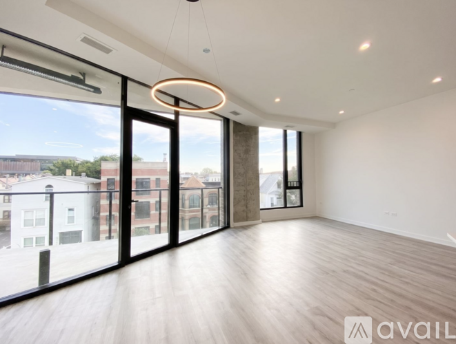 A spacious room with wooden flooring and large windows overlooking a cityscape.