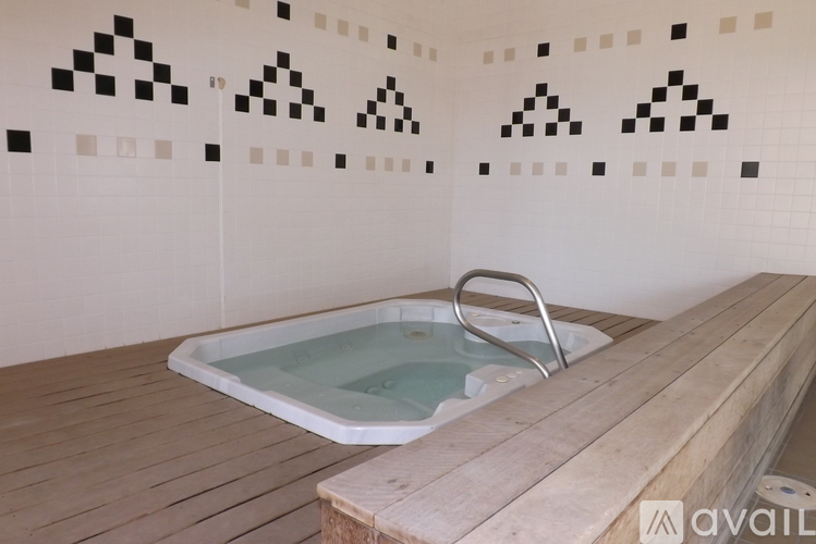 A hot tub sits on a wooden deck in a room with black and white tiles on the walls.