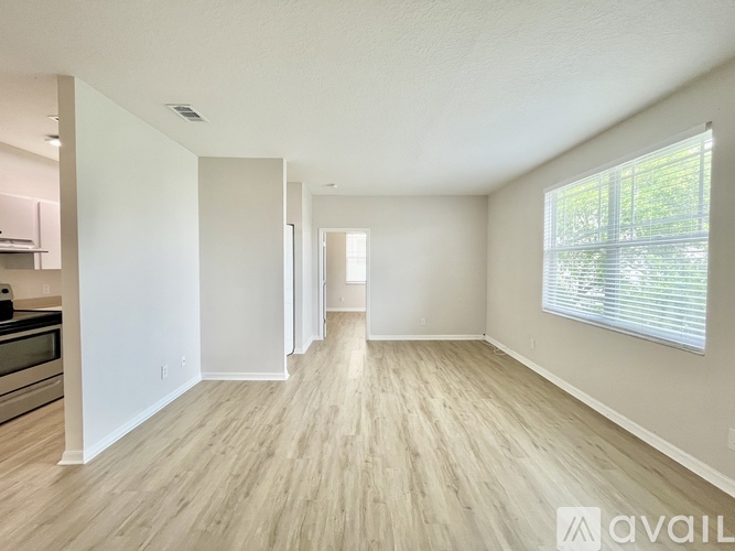 A spacious room with wooden flooring and a window with blinds.