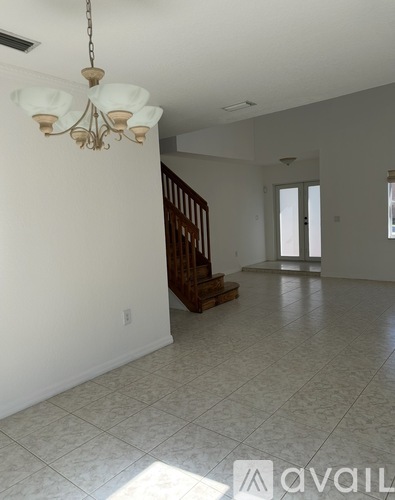 A chandelier hangs over a white tiled floor in a spacious room.