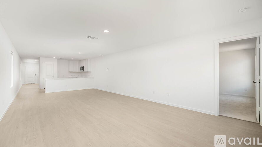 A spacious empty room with light wood flooring and white walls.