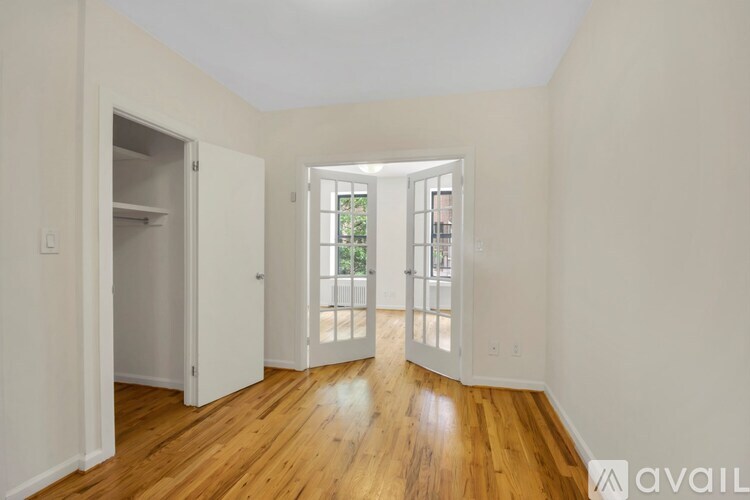 A room with wooden floors and white walls, with a door leading to a balcony.