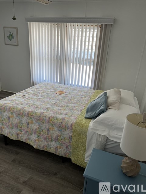 A bed with a floral patterned blanket and a blue pillow is in a room with a window covered in blinds.