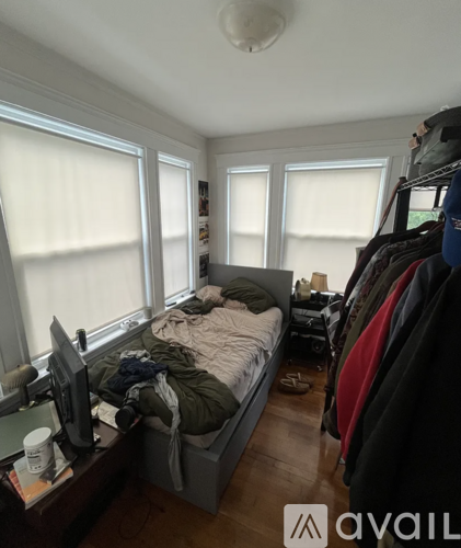 A bedroom with a bed, a desk with a computer monitor, and a clothing rack.