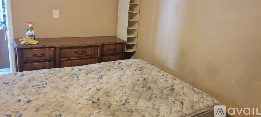A bed with a floral patterned cover sits in a room with a wooden dresser and a wall-mounted shelf.