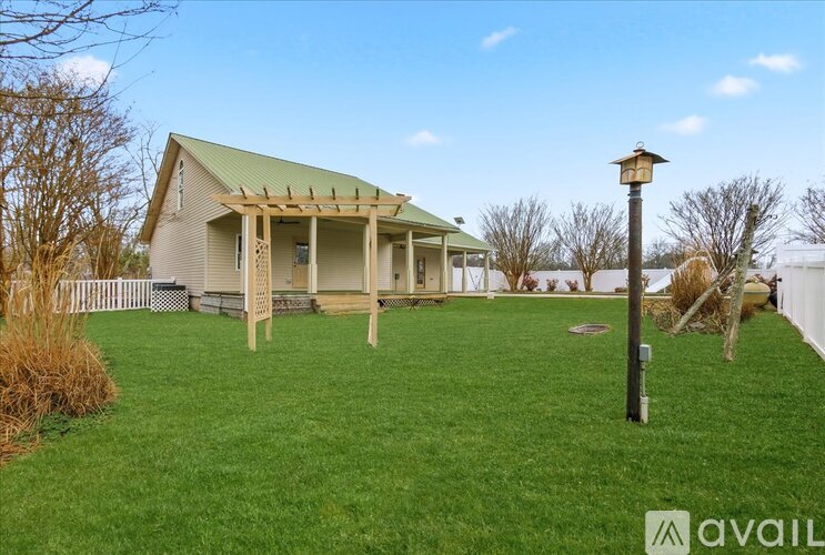 A house with a green roof and a porch is surrounded by a grassy yard.