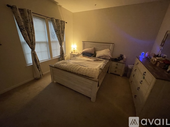 A well-lit bedroom with a large bed, nightstand, and window with curtains.