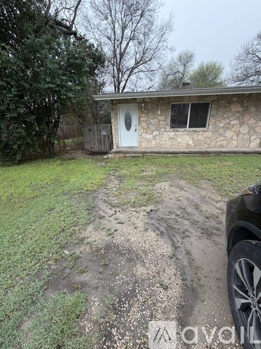 A house with a white door and a window is surrounded by grass and trees.