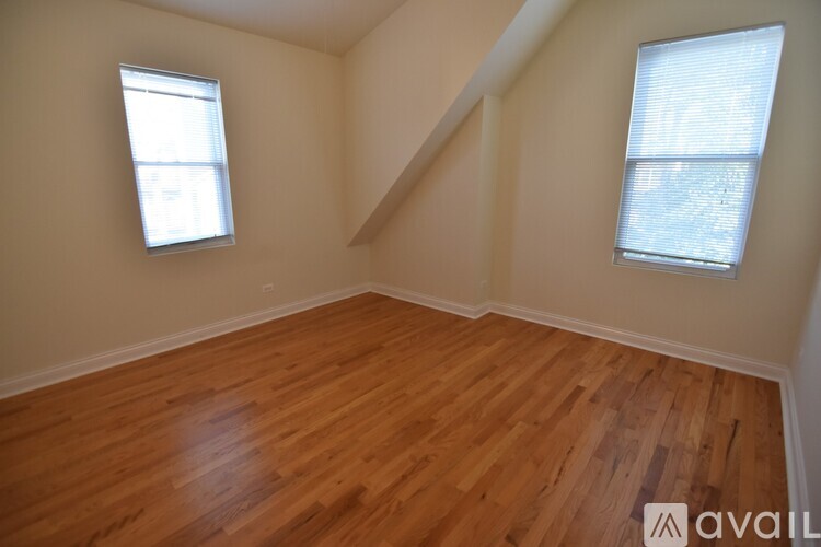 A room with wooden flooring and two windows.